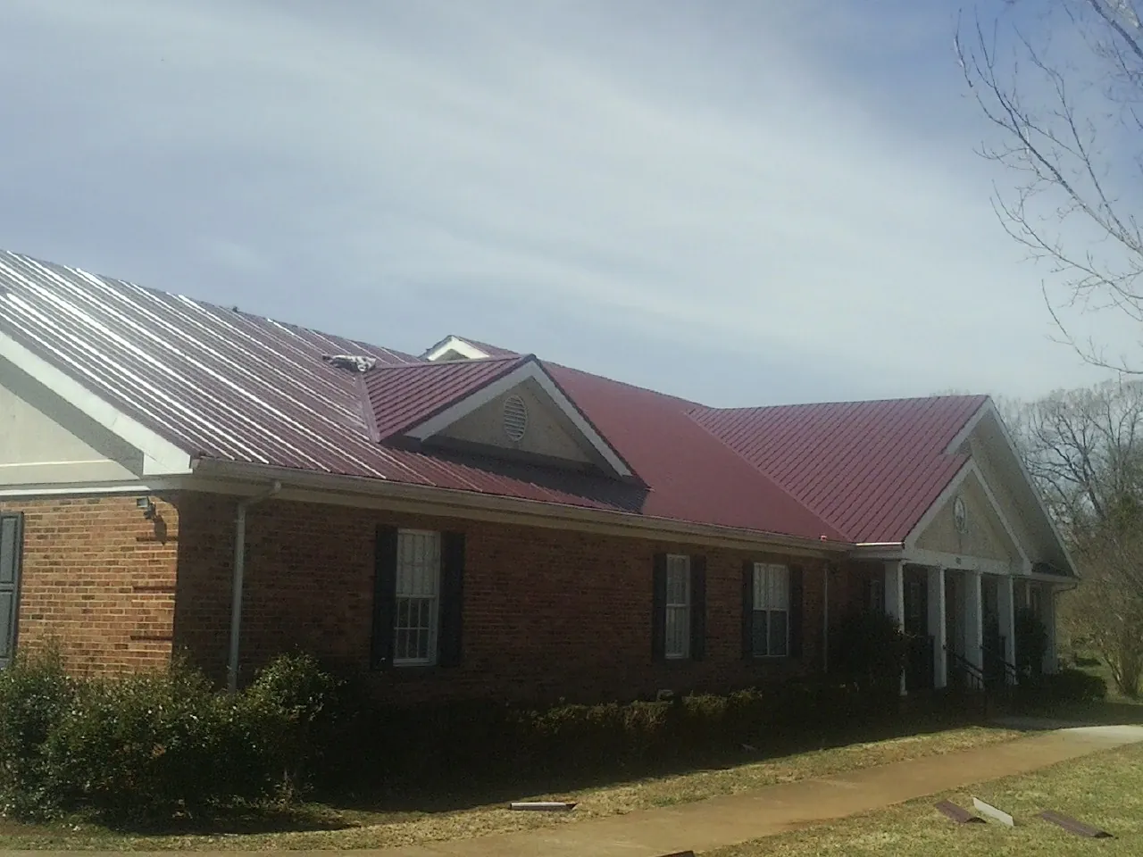 Red metal roof with gabled entries on a long brick building, from a Hail Damage Roof Repair job in Hatton