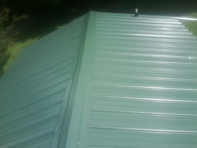 New green metal panels meeting at the ridge of a roof — Flat Roof Repair work by our crew in Hatton
