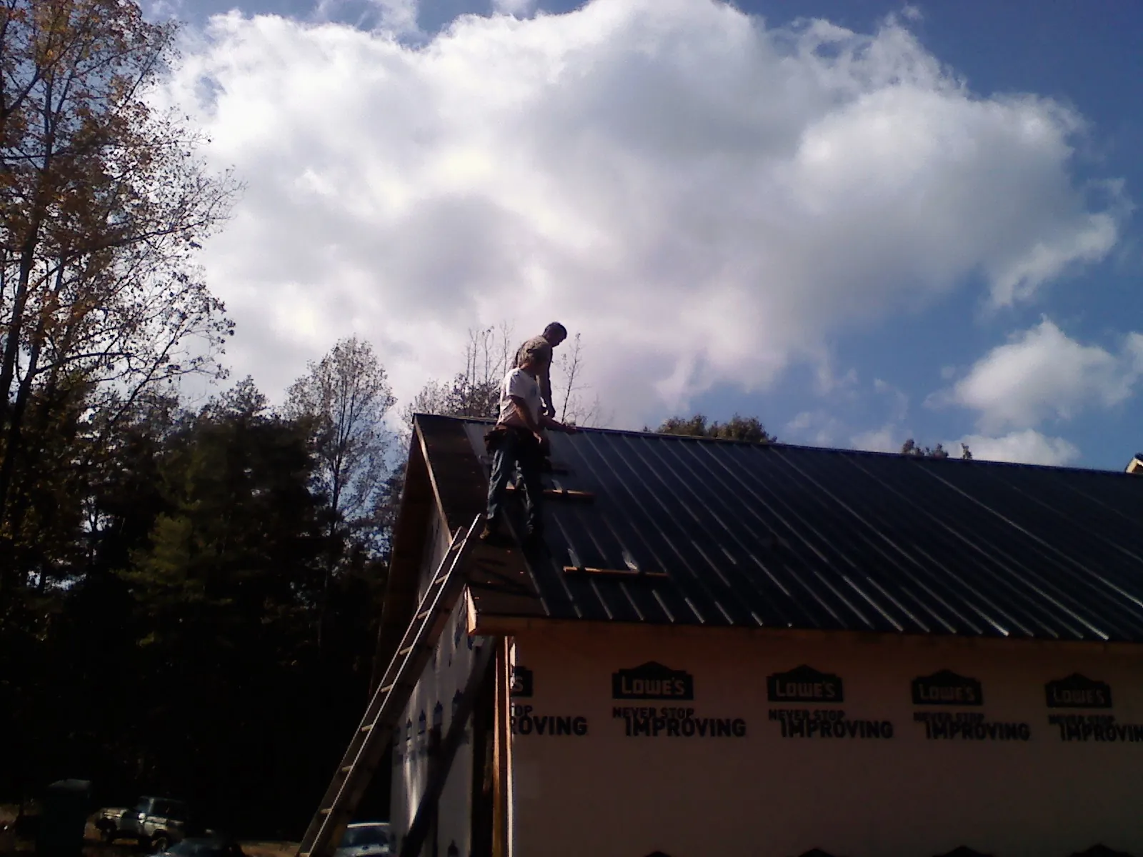 Roofer fastening dark metal panels high against a cloudy sky, from a Roof Inspection job in Hatton