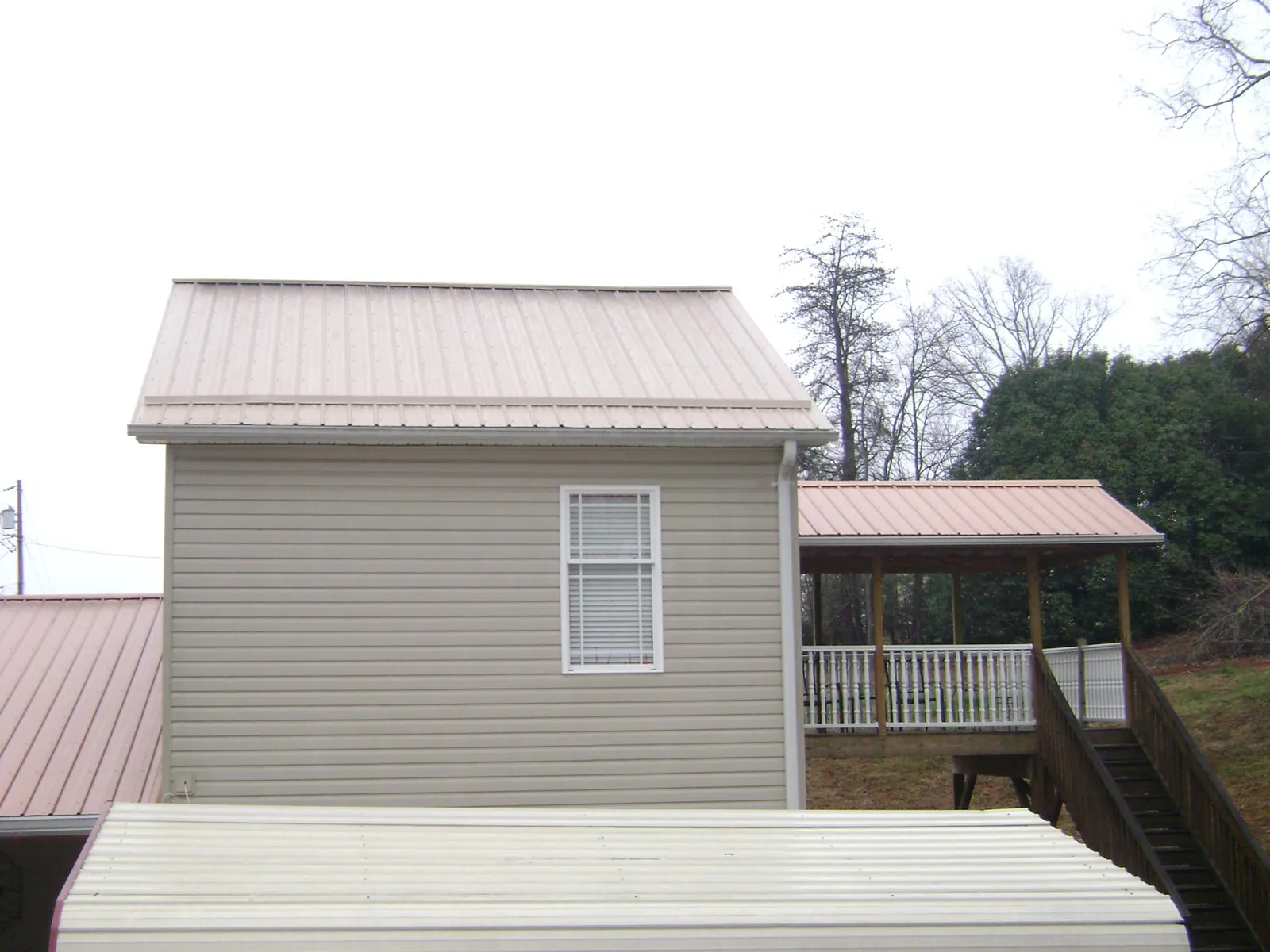 Tan metal roofs on a two story addition and attached porch, from a Roof Replacement job in Hatton